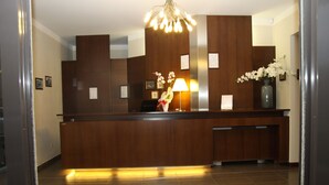 Un mostrador de recepción con detalles de madera, una lámpara de pie y un jarrón con flores blancas.