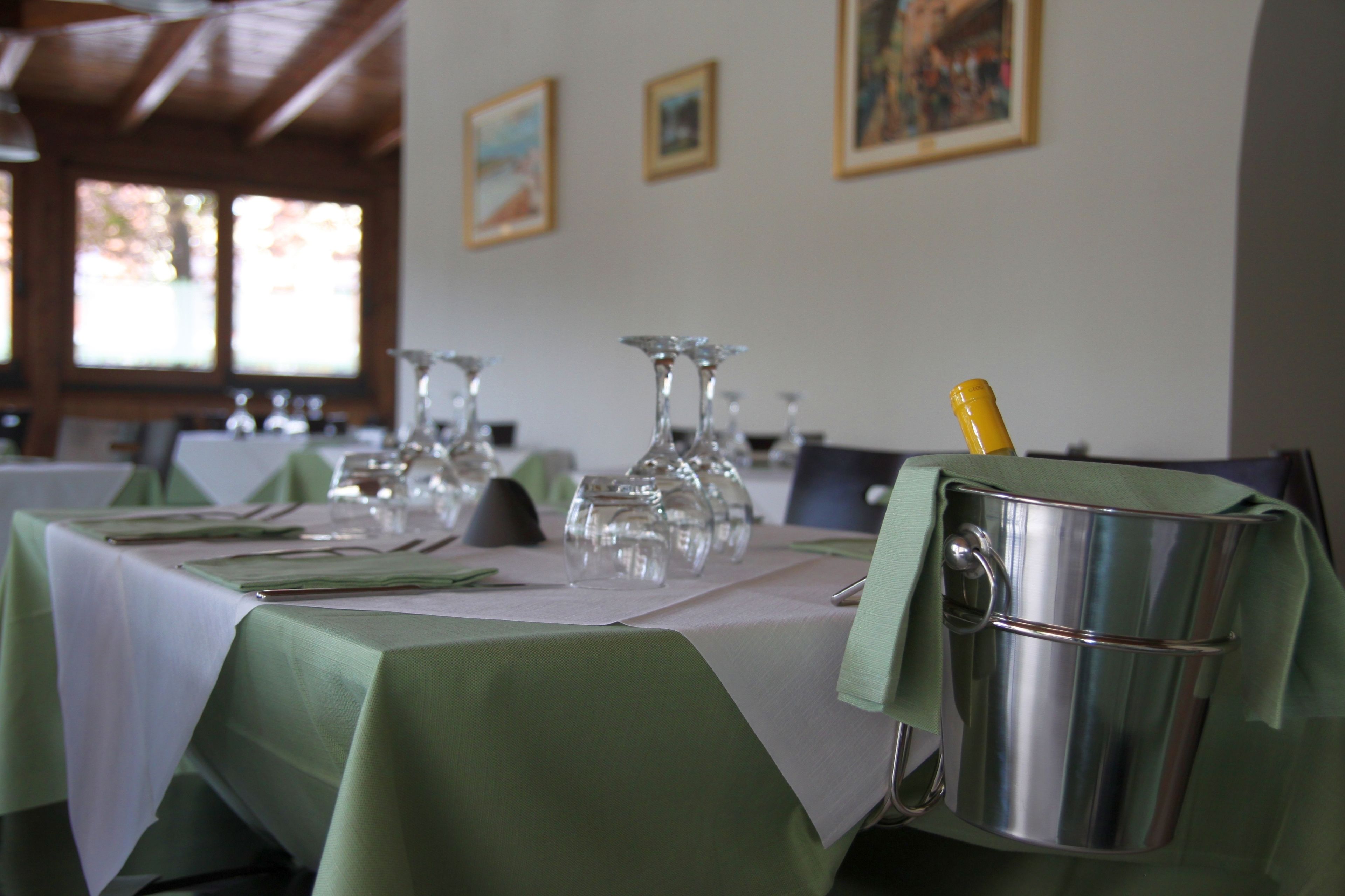 A dining table set with green tablecloths, clear glassware, and a champagne bottle in a metal bucket.