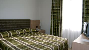 A hotel room with a bed, a bedside table with a lamp, a television, and a window with curtains.