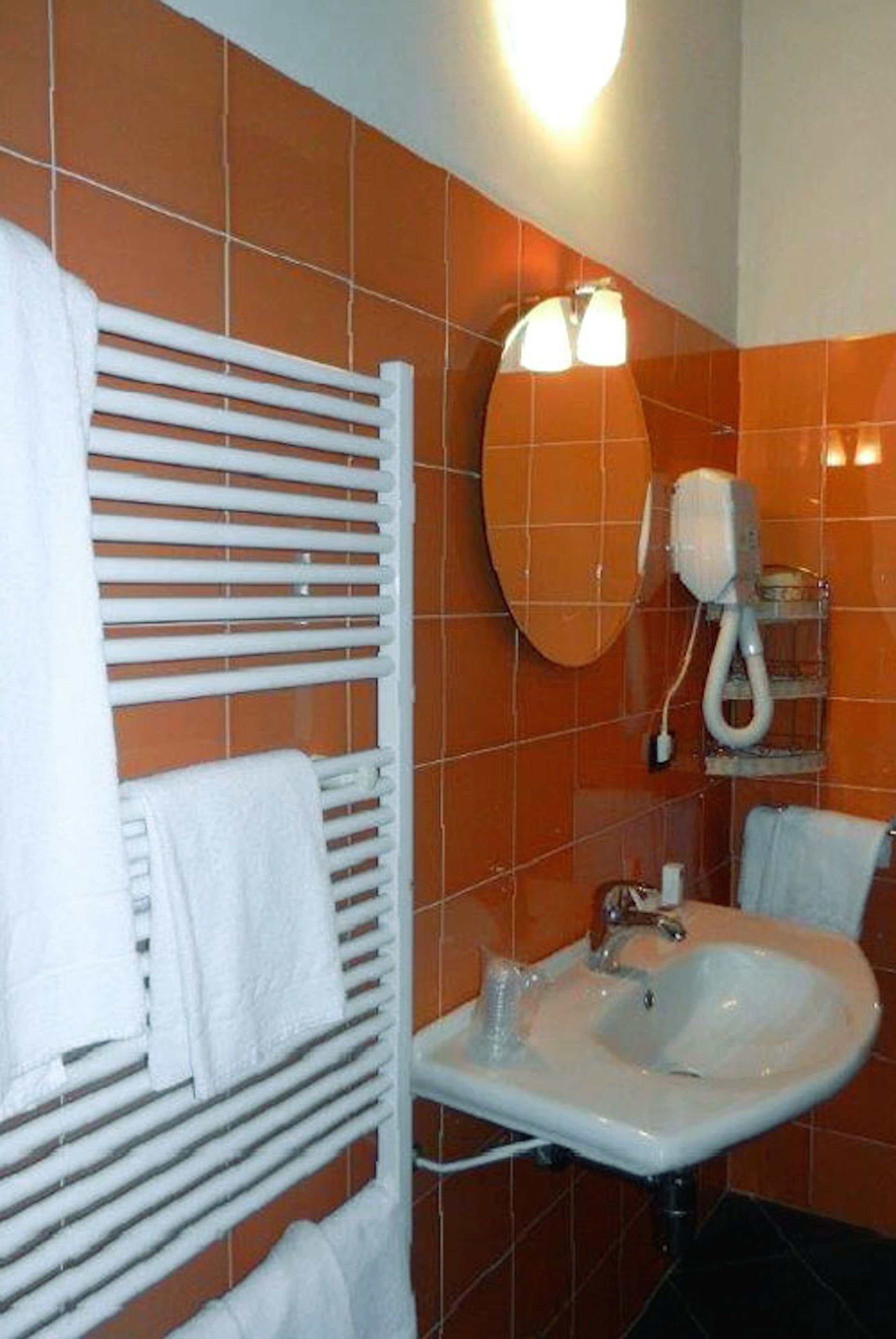 A bathroom with orange tiles, a white sink, a mirror, and a towel rack.