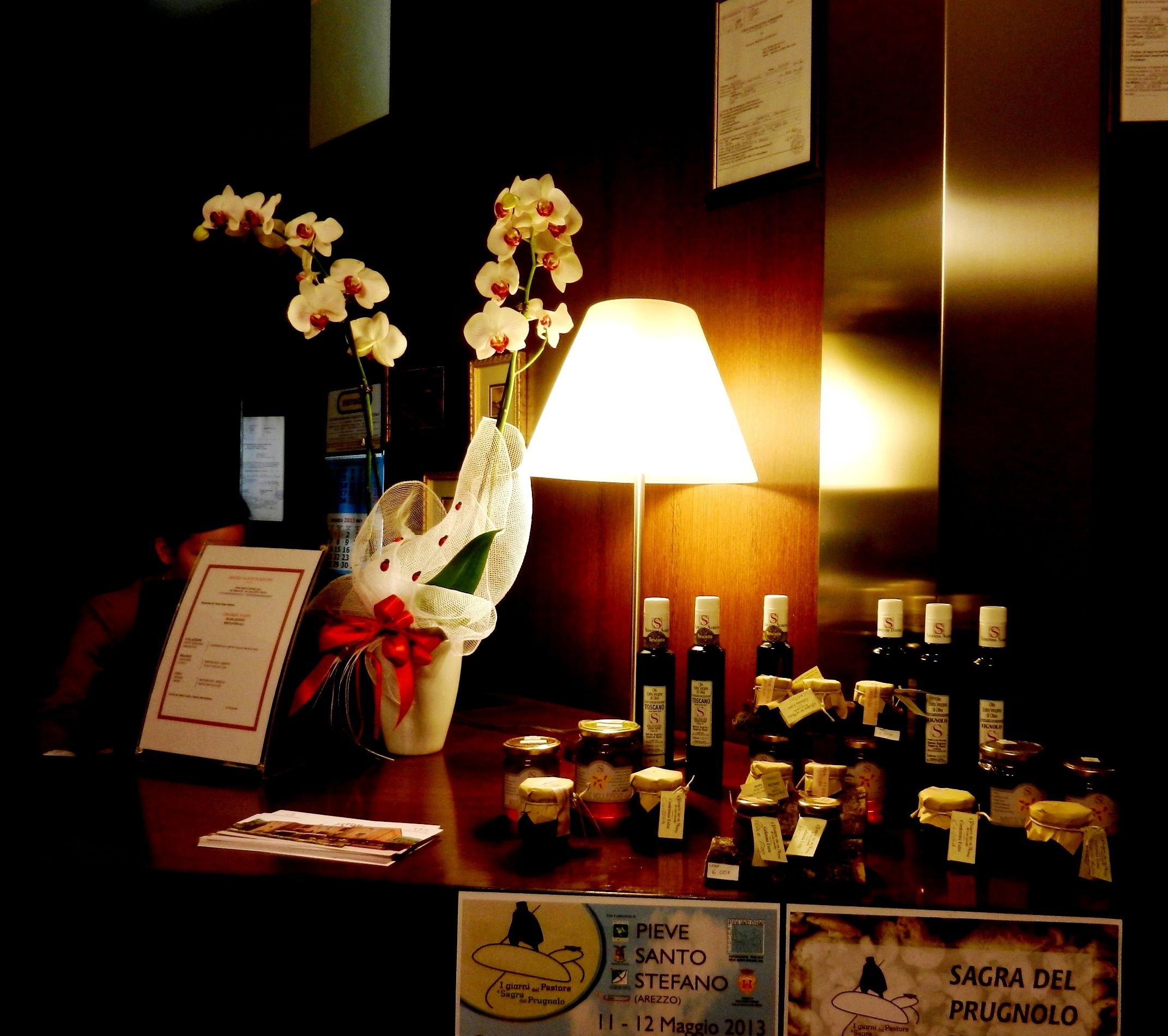 Een receptiebalie met een vaas witte orchideeën, een lamp en verschillende flessen wijn.