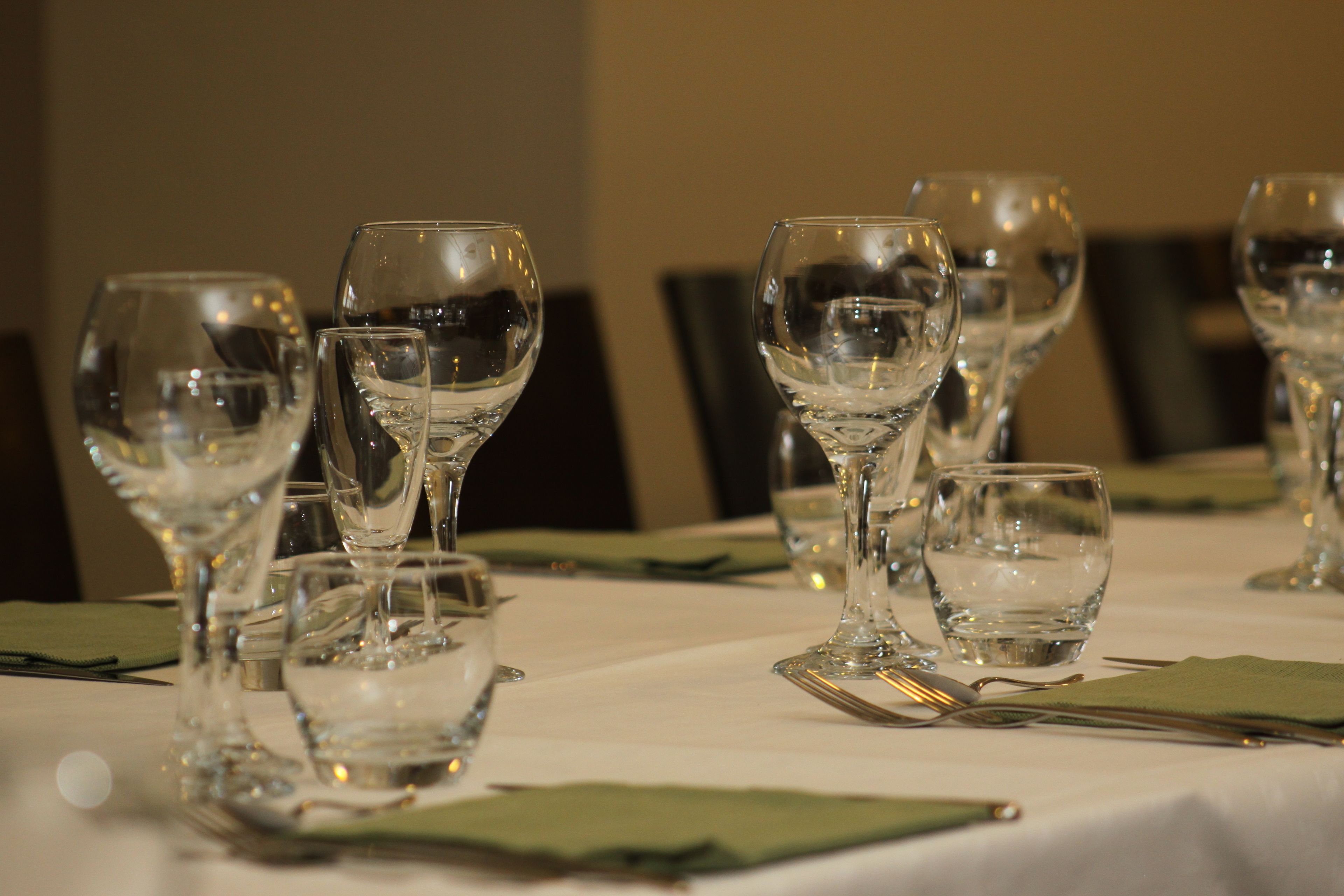 Una mesa dispuesta con varias copas de vino y vasos de agua, ordenada con servilletas verdes y cubiertos.
