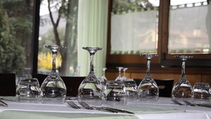 Una mesa dispuesta con varias copas de vino y cubiertos, con vistas a árboles y un edificio a través de una ventana.