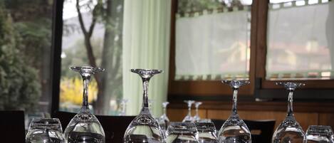 A table set with multiple wine glasses and cutlery, with a view of trees and a building through a window.