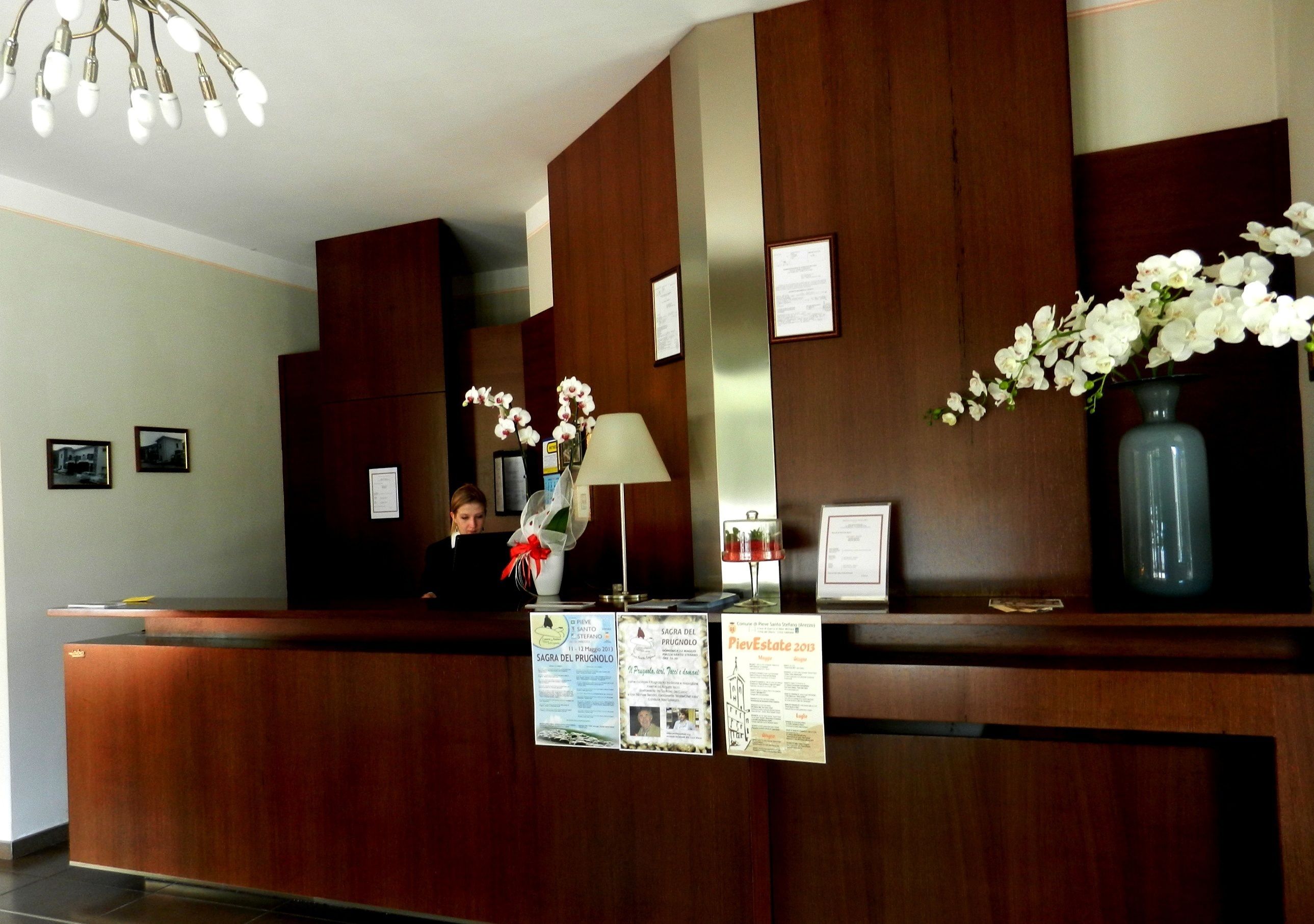 A reception desk with a wooden finish, a vase with white flowers, and informational posters.