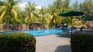 A swimming pool with palm trees, outdoor seating, and a stone wall. - Seri Malaysia Bagan Lalang (Sungai Pelek)