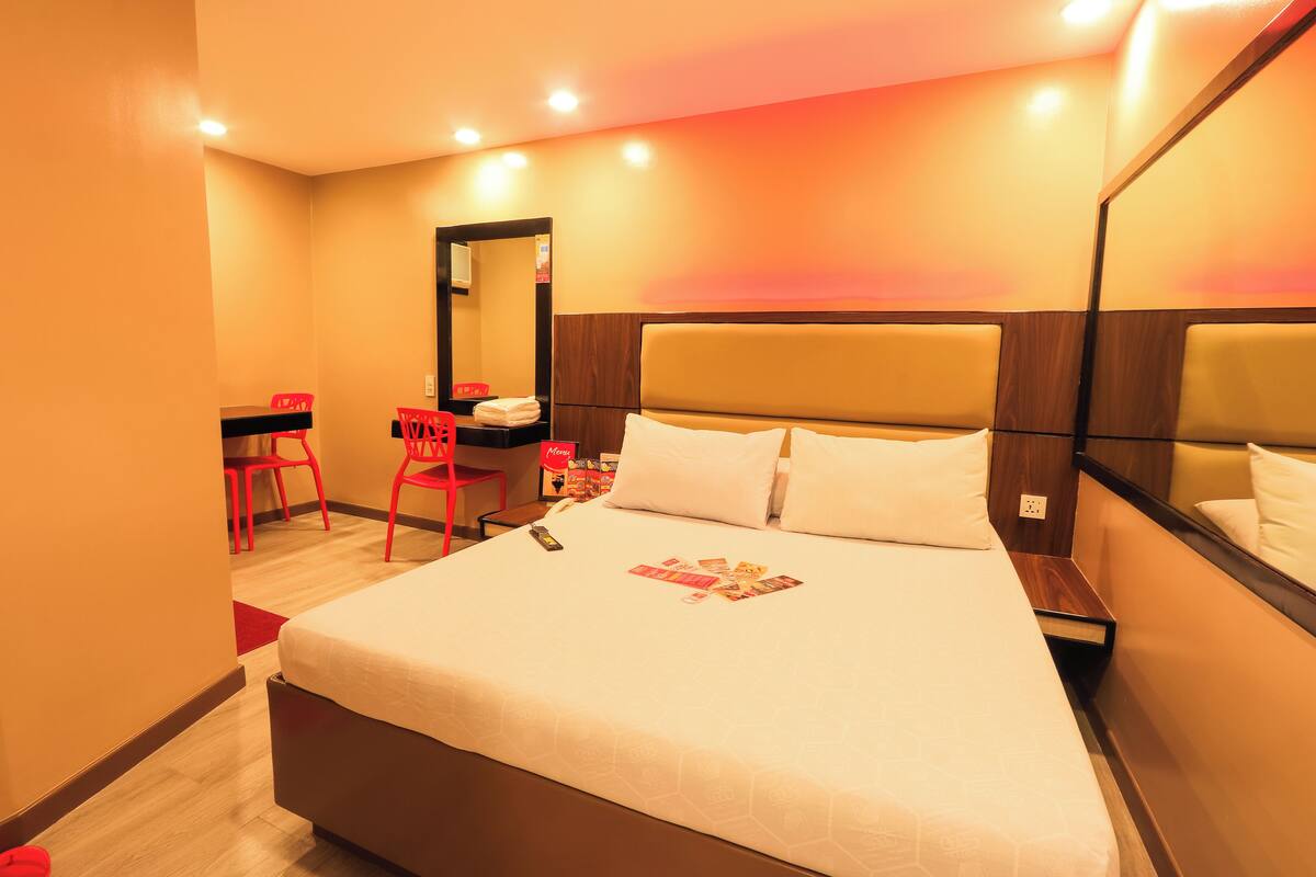A hotel room with a large bed, a desk with a chair, and a mirror.