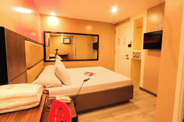 A hotel room with a bed, a desk with a chair, a mirror, a TV, and a door. - Hotel Sogo Alabang Rotonda (Muntinlupa)