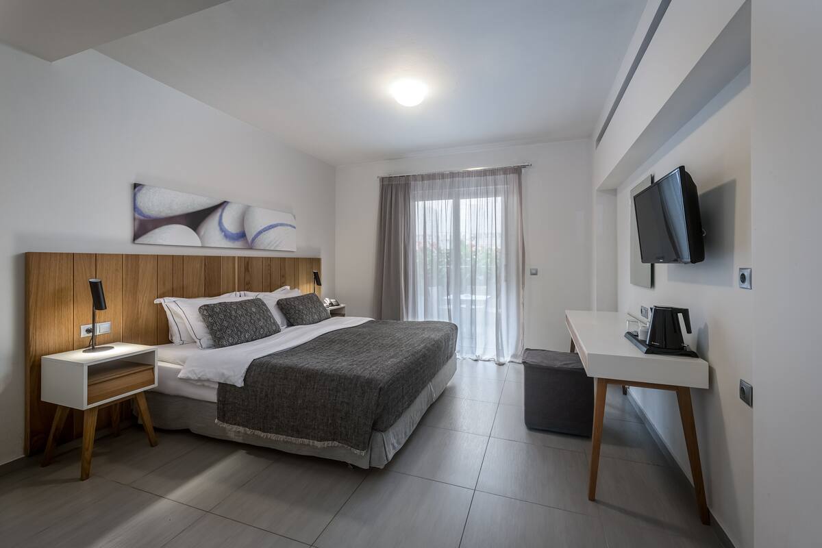 Quarto de hotel moderno com uma cama grande, mesas de cabeceira, uma escrivaninha e uma televisão.