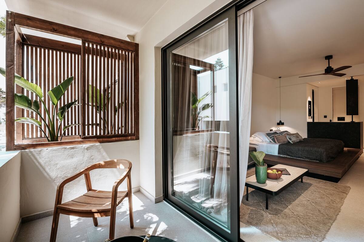Uma sala de estar moderna com um sofá, uma mesa de centro e uma poltrona perto de uma janela grande com vista para o exterior.
