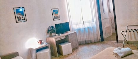 Una habitación con cama, escritorio, silla, televisor y ventana con cortinas.