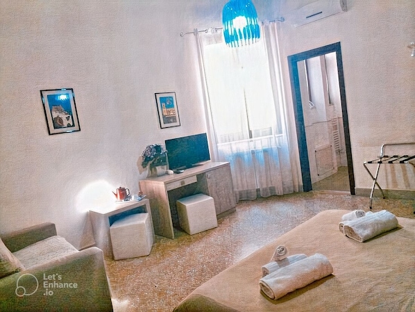 A room with a bed, a desk, a chair, a TV, and a window with curtains.