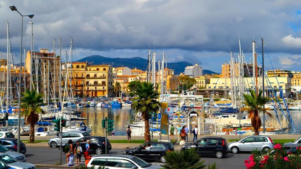 A marina with numerous boats docked, surrounded by buildings and palm trees. - Il Quadrifoglio Room&Suite (Palermo)
