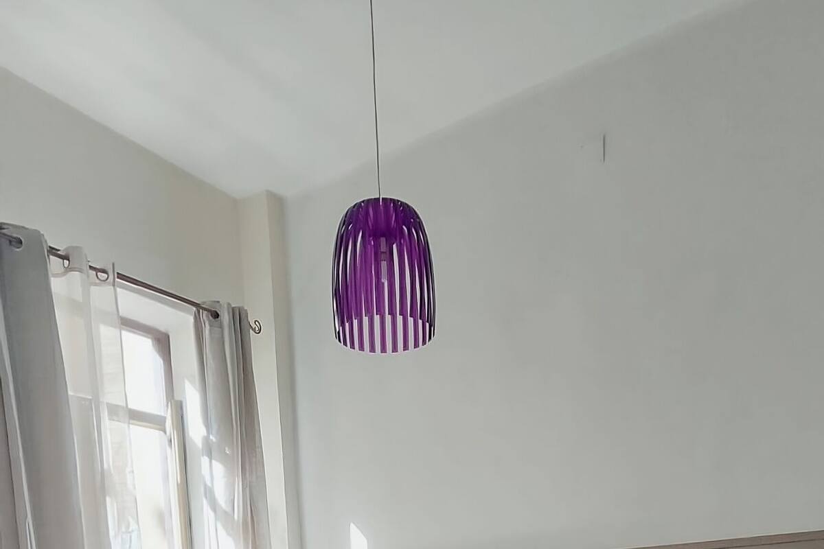 Ein Schlafzimmer mit Bett, Holzboden, einer Hängelampe und einem Fenster mit Vorhängen.