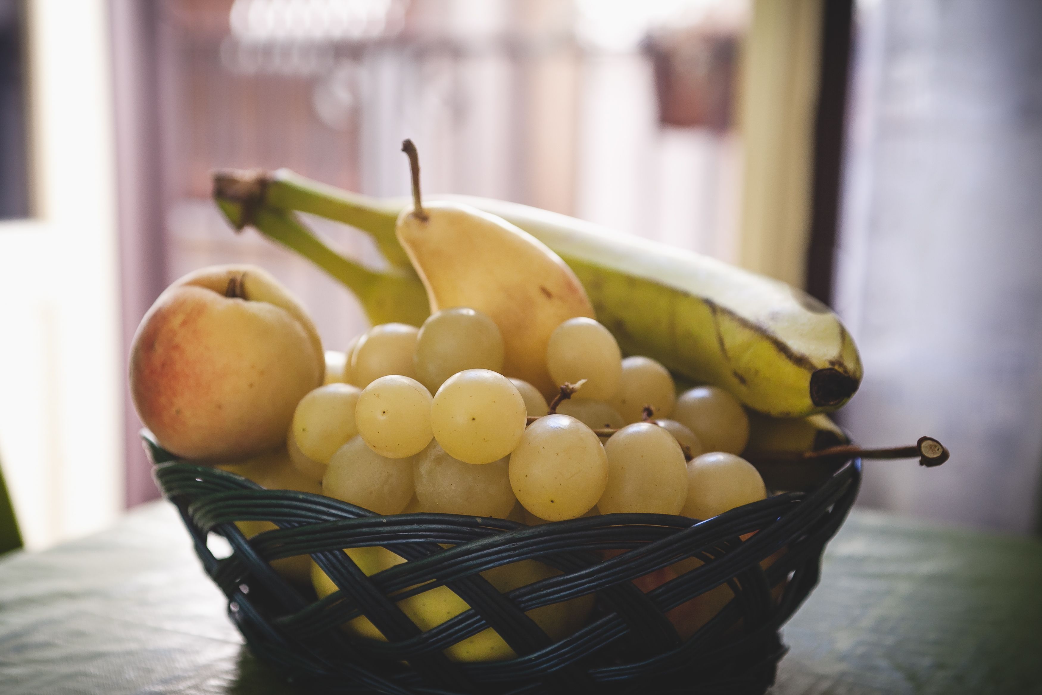 A wicker basket containing a variety of fruits including bananas, apples, and grapes.