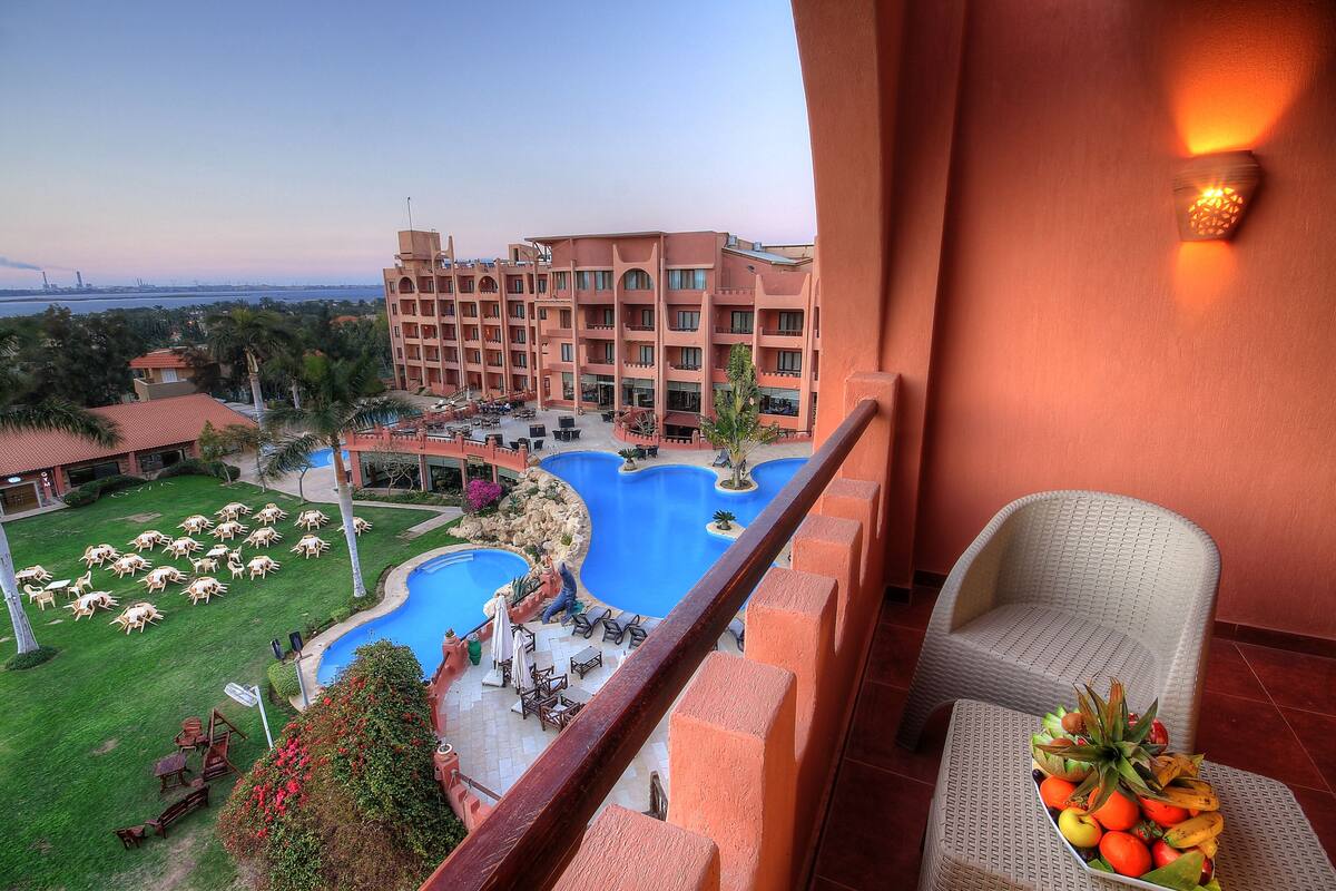 A balcony with a view of a swimming pool, lounge chairs, and a fruit bowl.