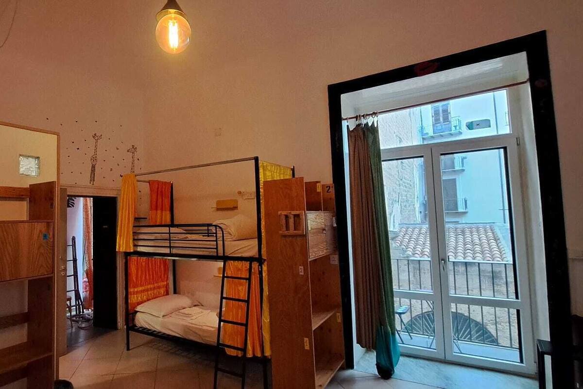Un dormitorio con literas, un armario de madera, una escalera y una ventana con vistas a edificios.