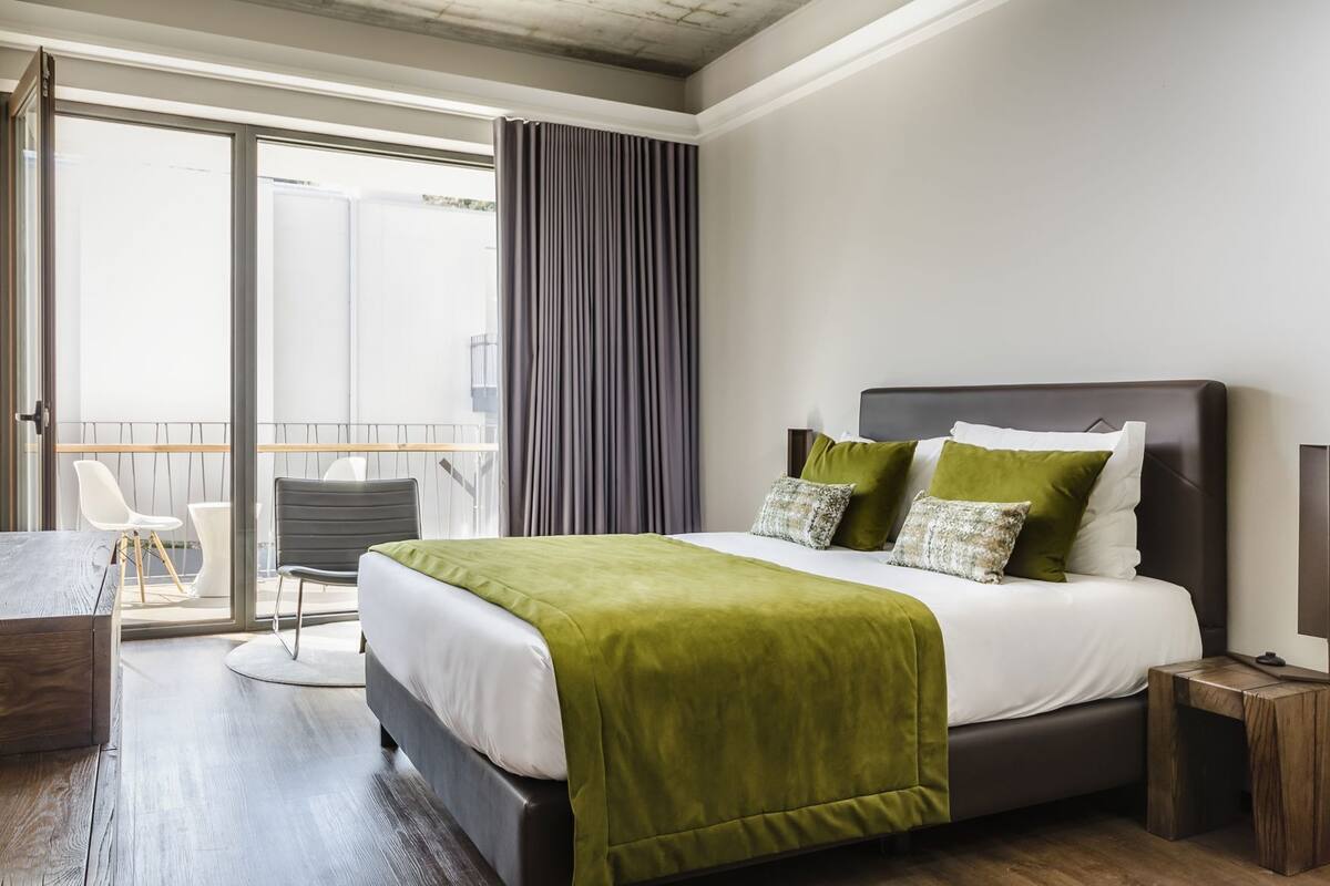 Een moderne hotelkamer met een groot bed, een balkon met een stoel en een houten bureau.
