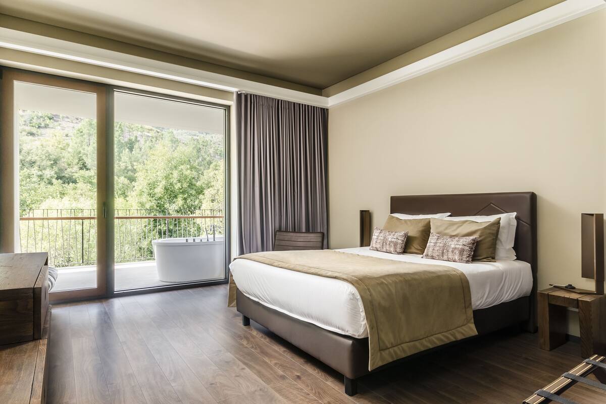 Een slaapkamer met een groot bed, een houten bureau en uitzicht op groen via een schuifdeur.