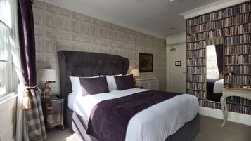 A neatly arranged bedroom with a large bed, a bedside table, a nightstand, a bookshelf, and a mirror.