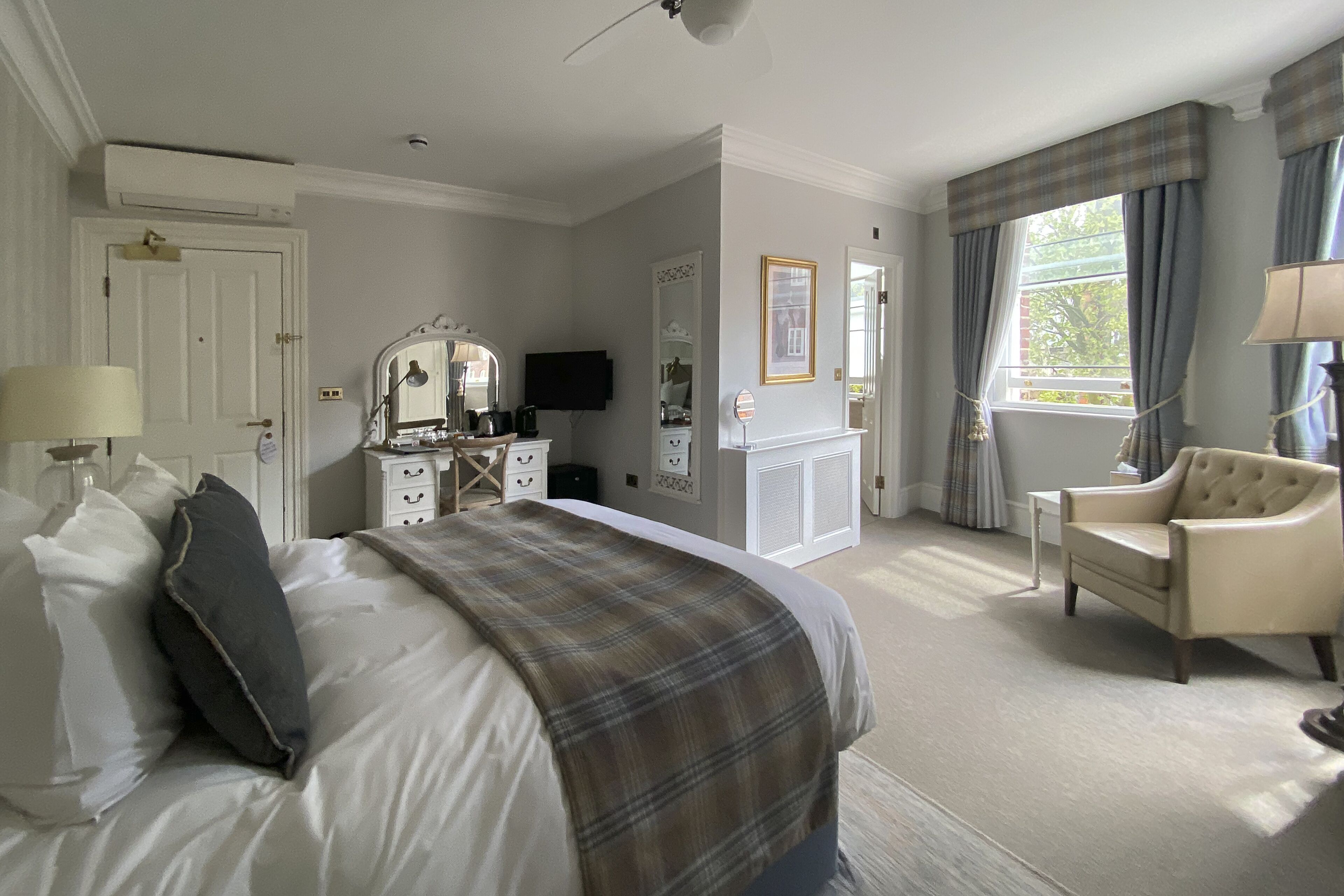 Une chambre d’hôtel avec un grand lit, une chaise, une commode, un téléviseur et une fenêtre avec des rideaux.