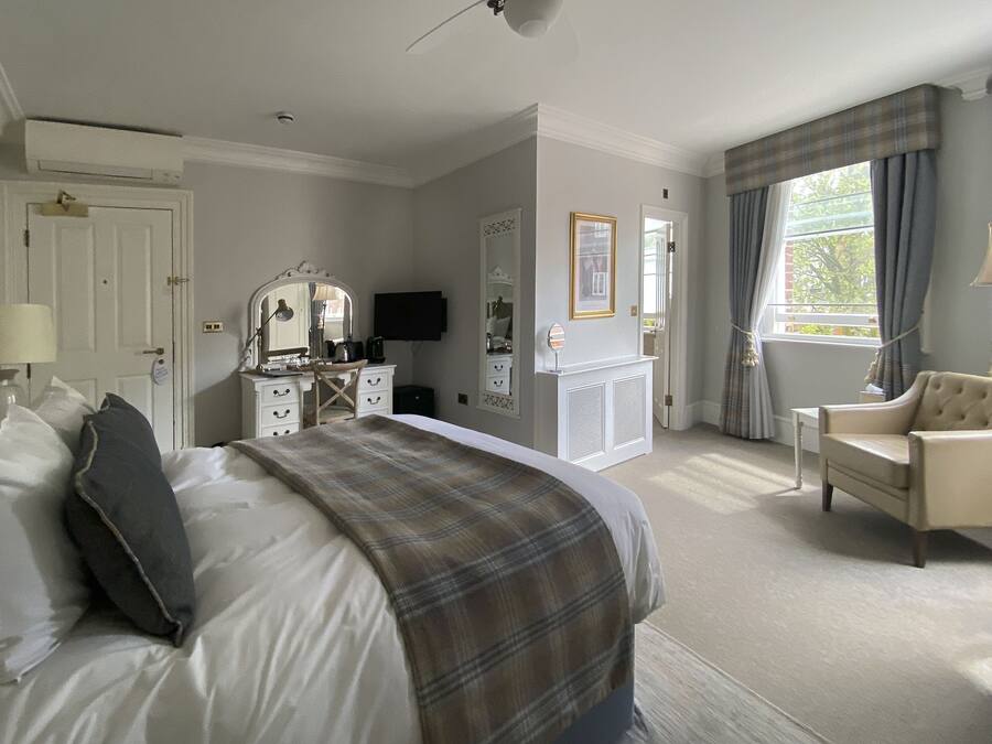 Une chambre d’hôtel avec un grand lit, une chaise, une commode, un téléviseur et une fenêtre avec des rideaux.