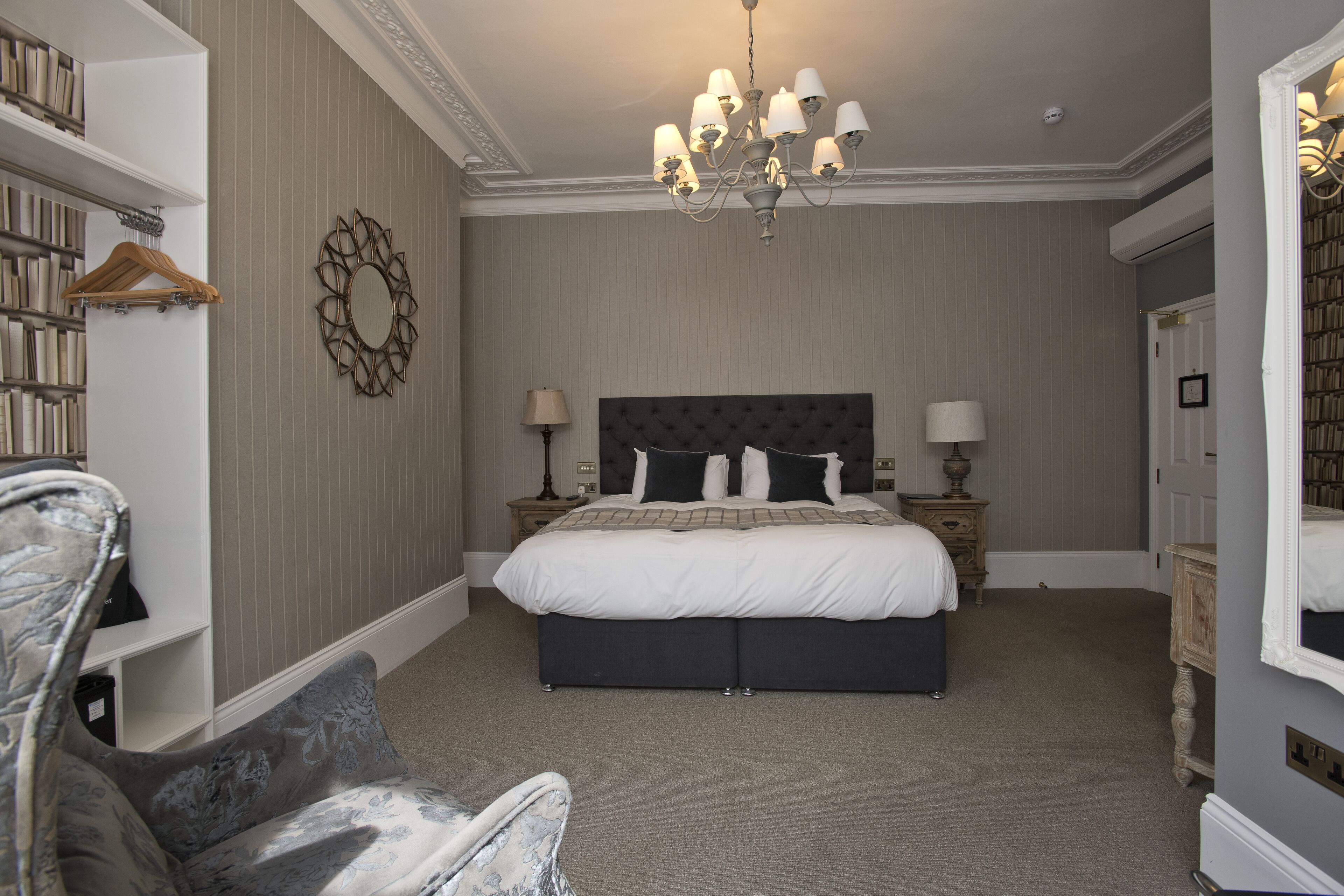 A bedroom with a large bed, a chandelier, a dresser, and a bookshelf.