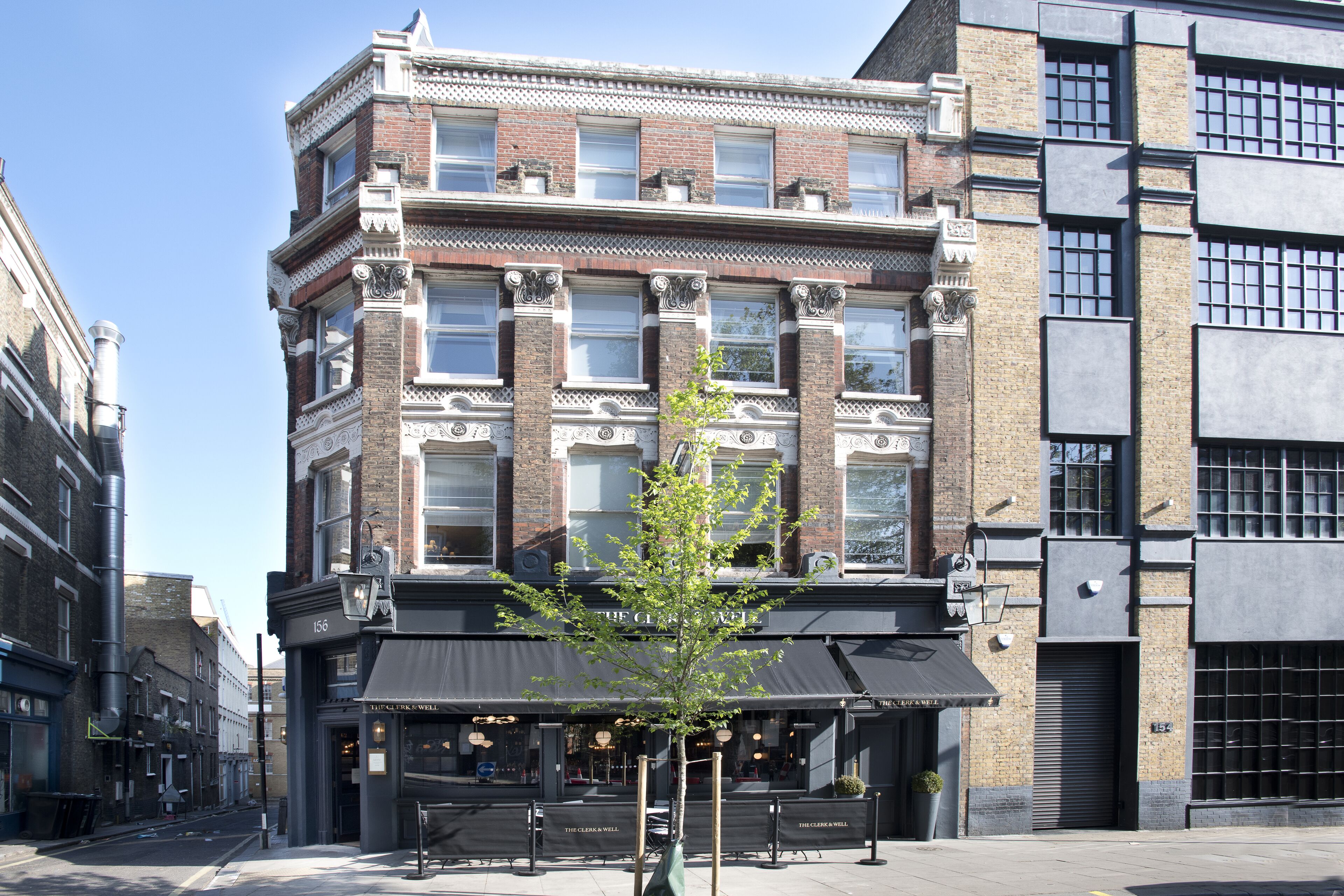 A corner building with a black awning, a tree in front, and a sign reading "The Claw Well".
