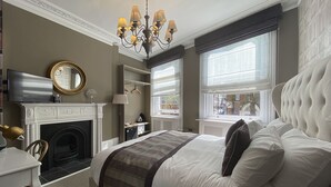 A bedroom with a large bed, a fireplace, a chandelier, and a view of the street through the window. - The Clerk & Well Pub & Rooms (London)