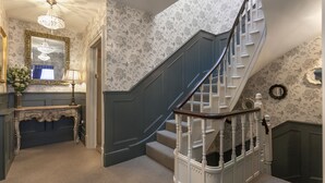 A staircase with white balusters and a dark blue handrail, leading to a landing with a mirror and a lamp. - The Clerk & Well Pub & Rooms (London)