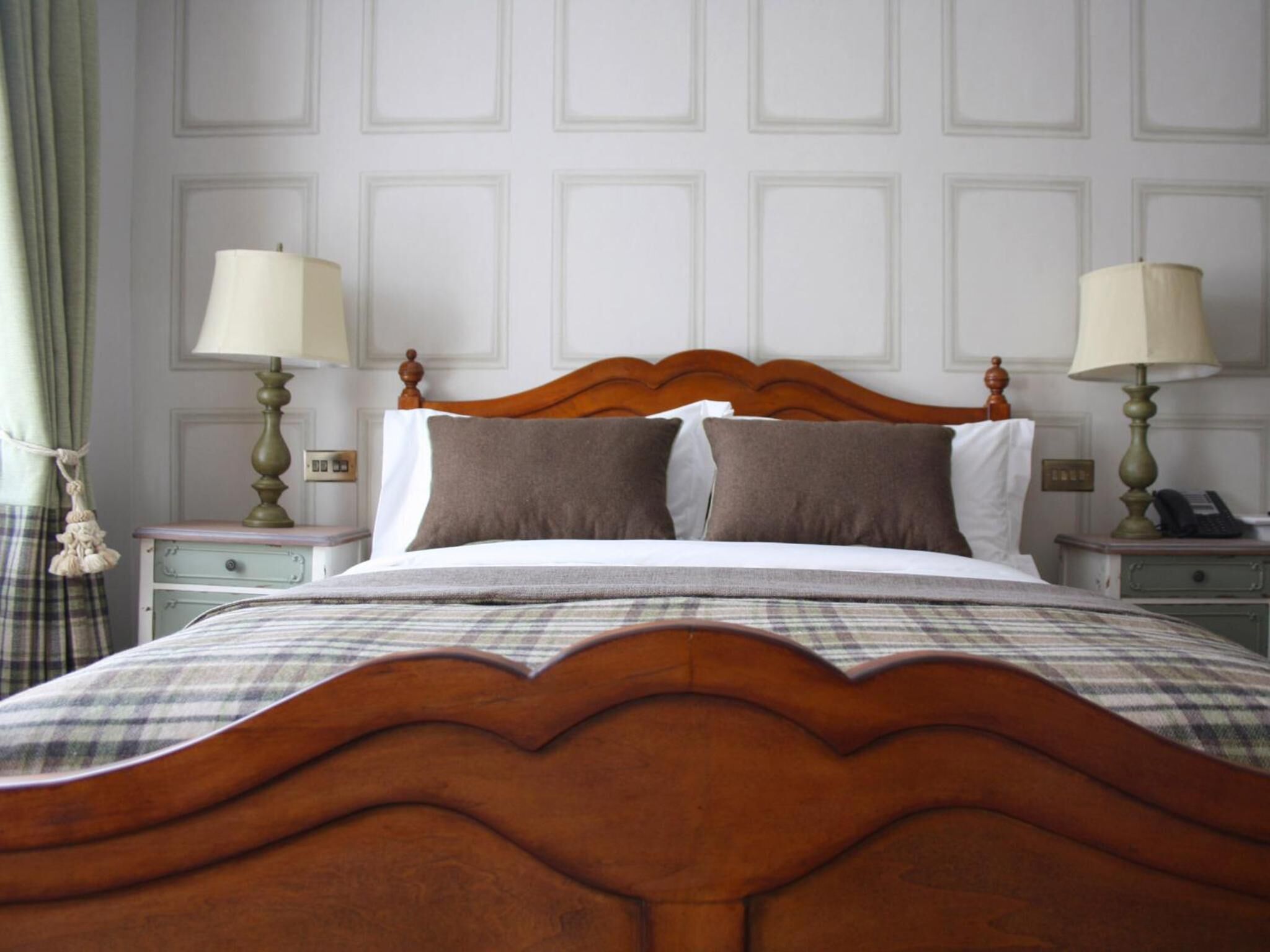 A neatly made bed with a wooden headboard, two bedside tables with lamps, and a plaid bedspread.