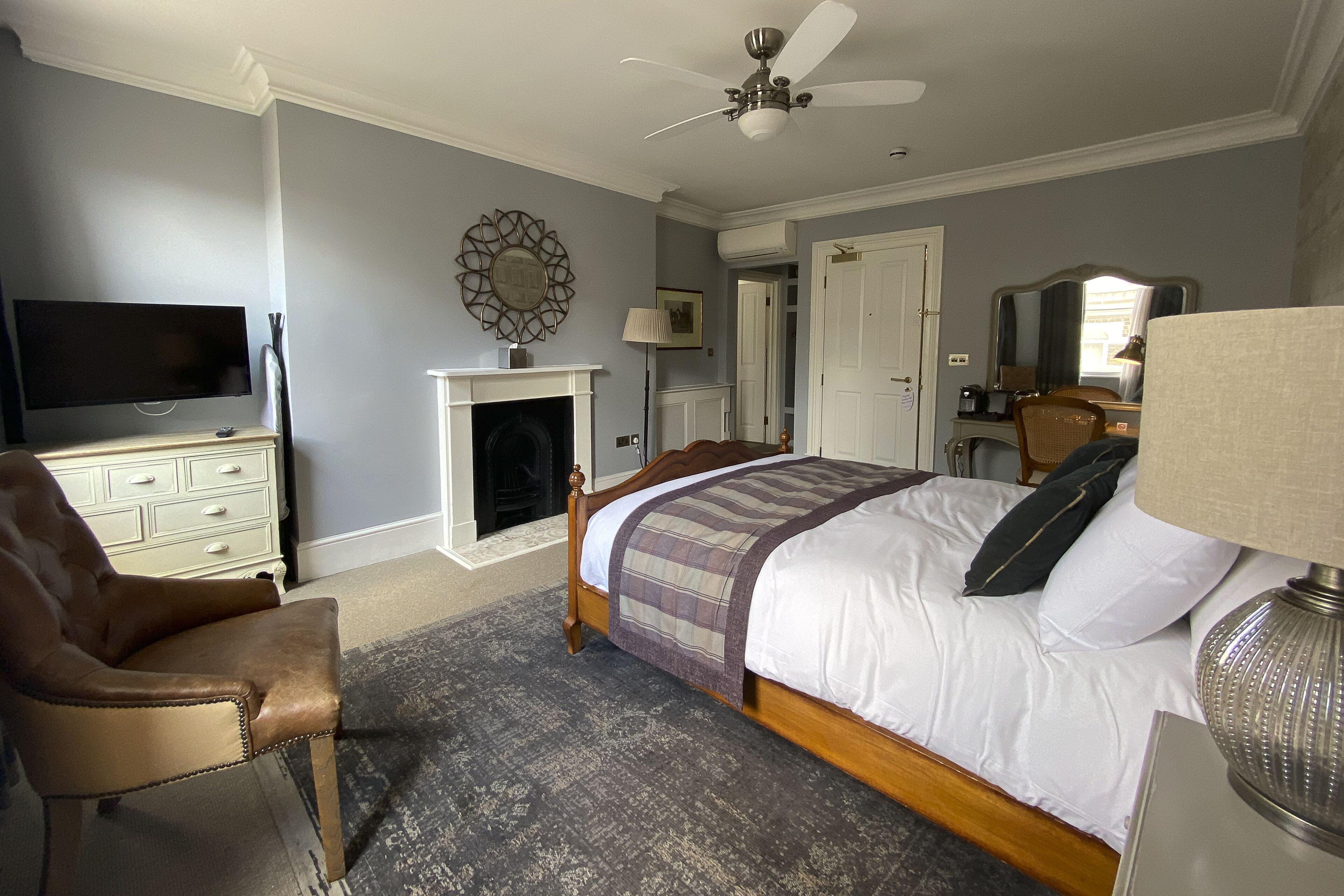 A bedroom with a bed, a television, a fireplace, a ceiling fan, and a chair.
