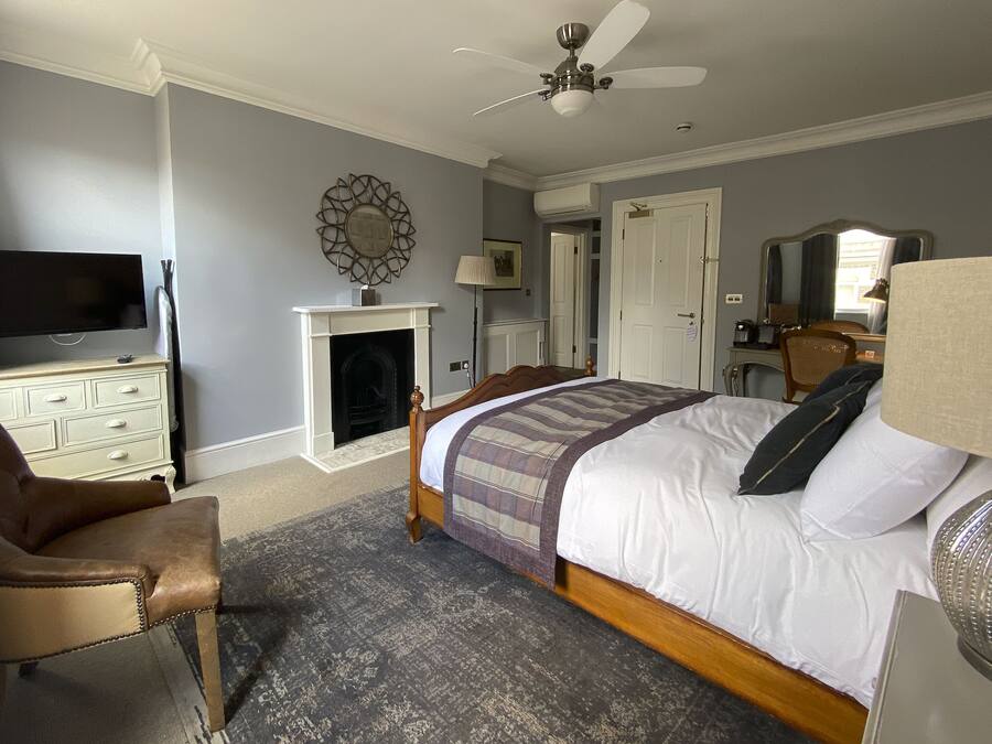 A bedroom with a bed, a television, a fireplace, a ceiling fan, and a chair.