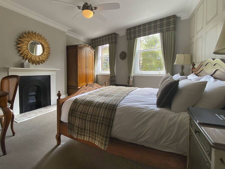 A bedroom with a bed, a dresser, a chair, a fireplace, and a window with curtains.