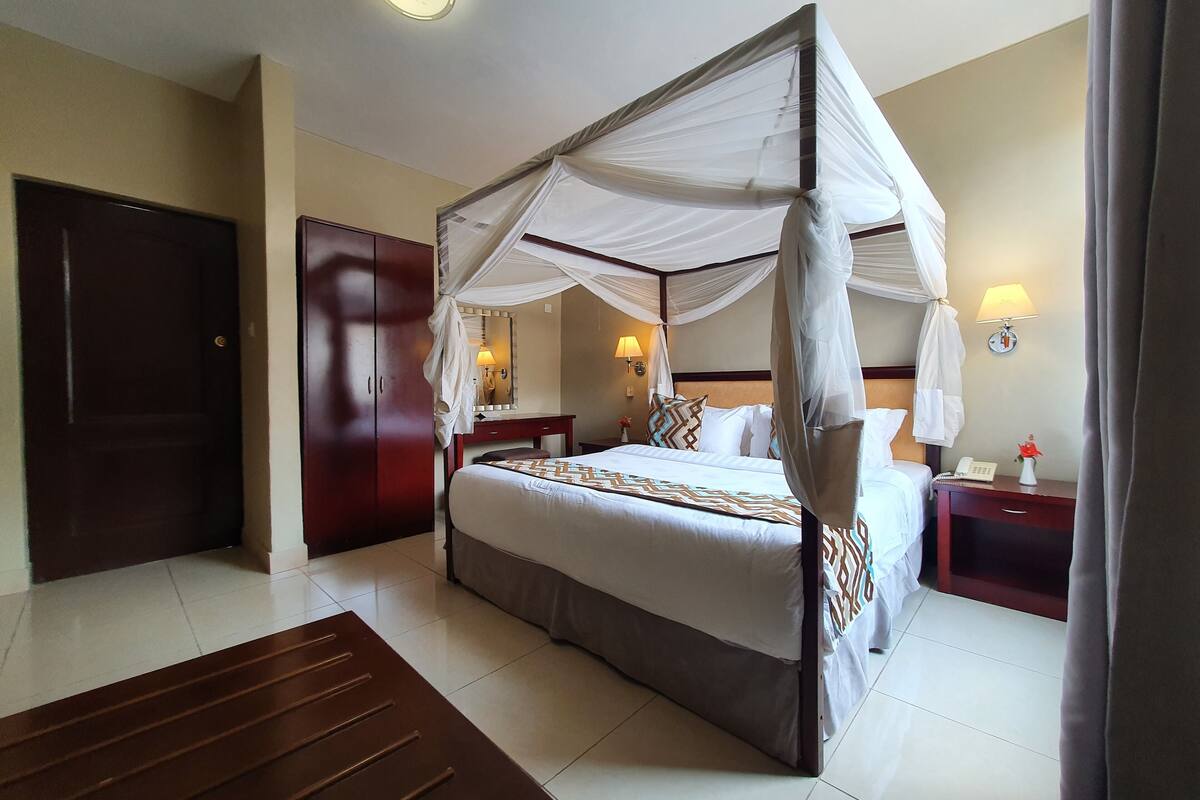 Habitación de hotel con cama con dosel, un escritorio de madera, una mesita de noche, una lámpara y una puerta.