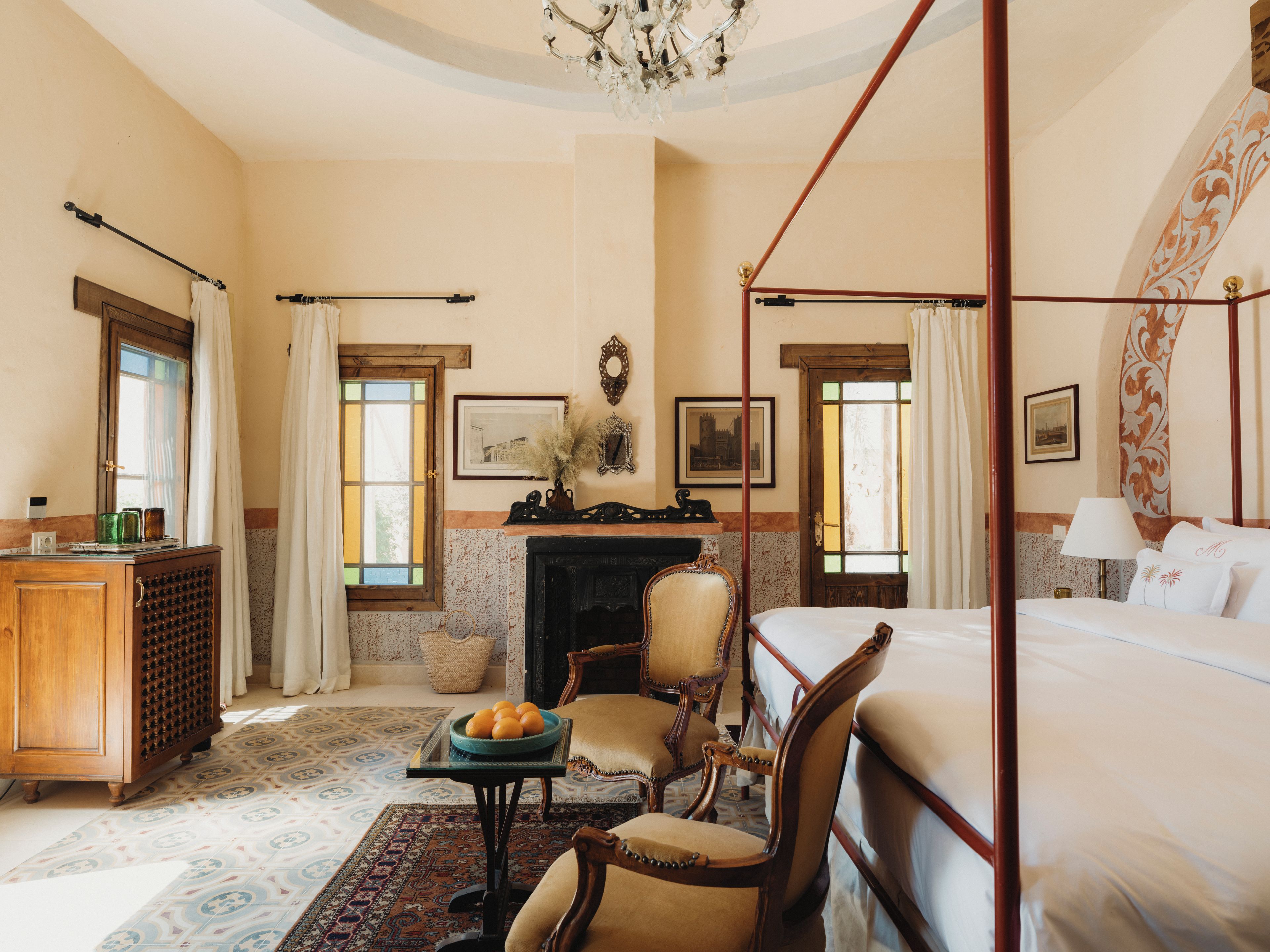 A four-poster bed with a canopy, a fireplace, a wooden desk, and a chair.