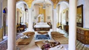 A spacious room with a large bed, multiple seating areas, and a chandelier. - Al Moudira Hotel (Luxor)