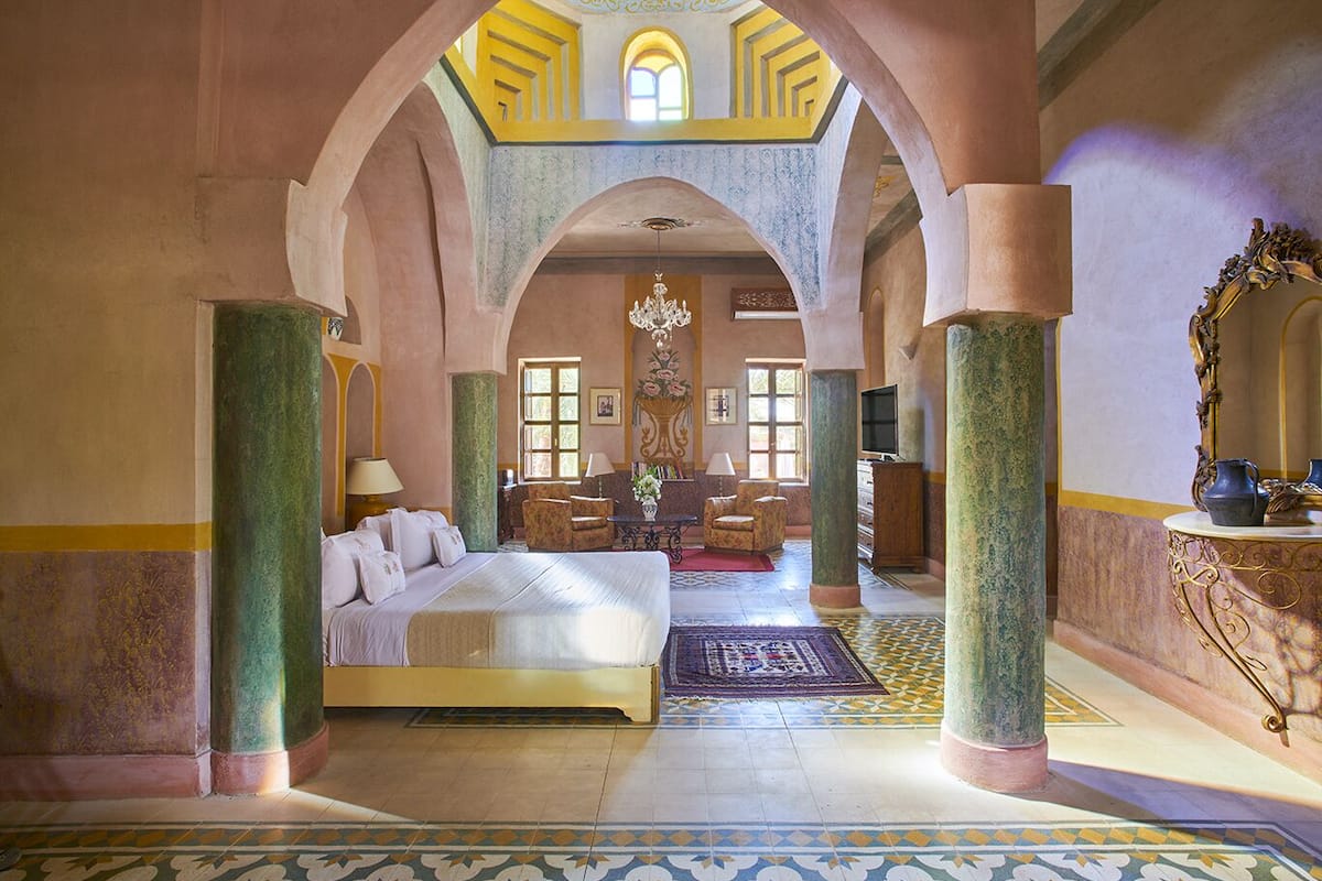 A spacious room with a large bed, a chandelier, and a view through an arched doorway.