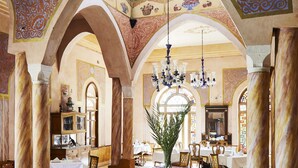 A spacious dining area with high ceilings, ornate arches, and a chandelier. Tables are set with white tablecloths and chairs. - Al Moudira Hotel (Luxor)