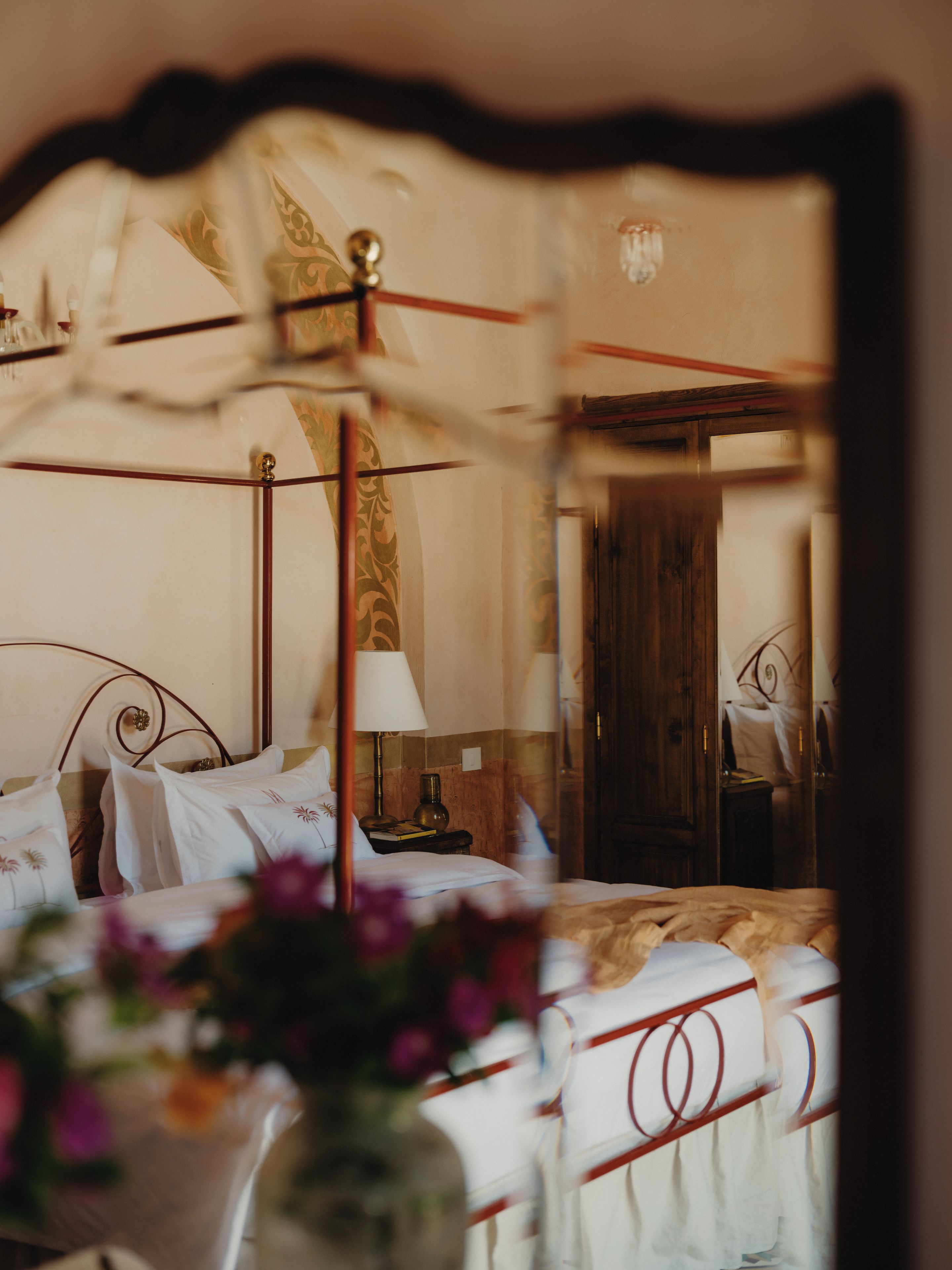 Una camera da letto con un letto a baldacchino, un comodino con una lampada e uno specchio che riflette la stanza.