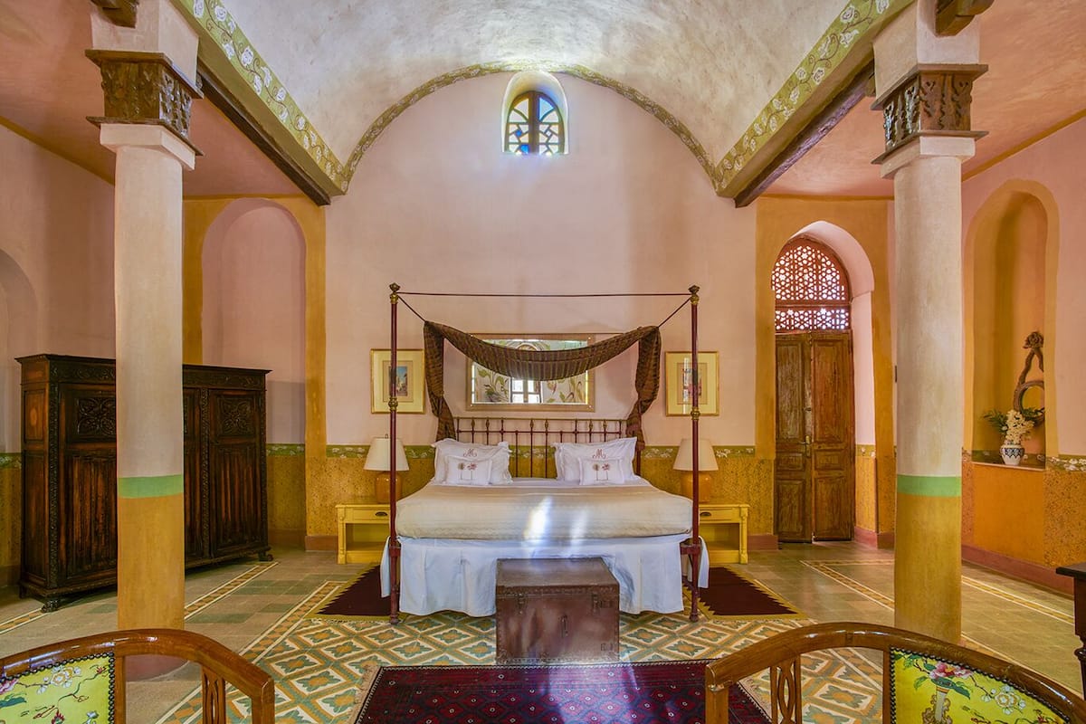 A spacious bedroom with a four-poster bed, a large window, and a decorative ceiling.