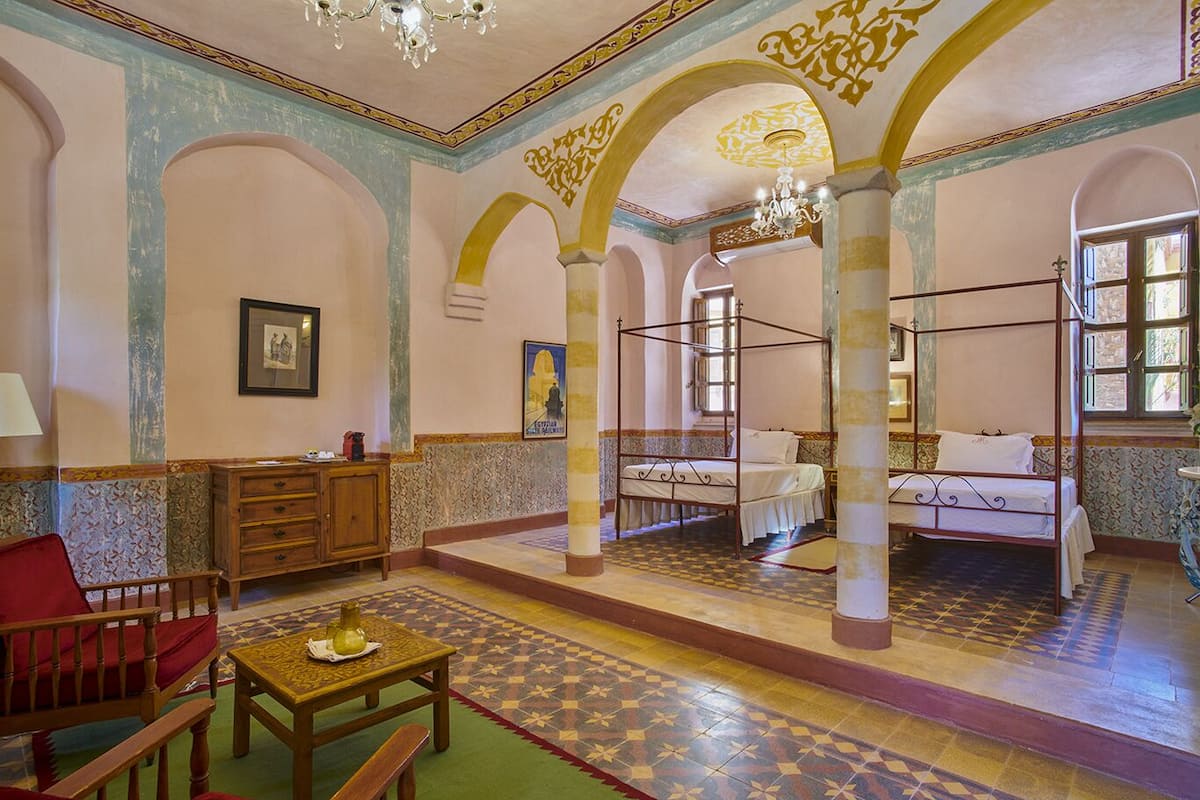 A room with a four-poster bed, a wooden cabinet, a red chair, and a table with a vase.