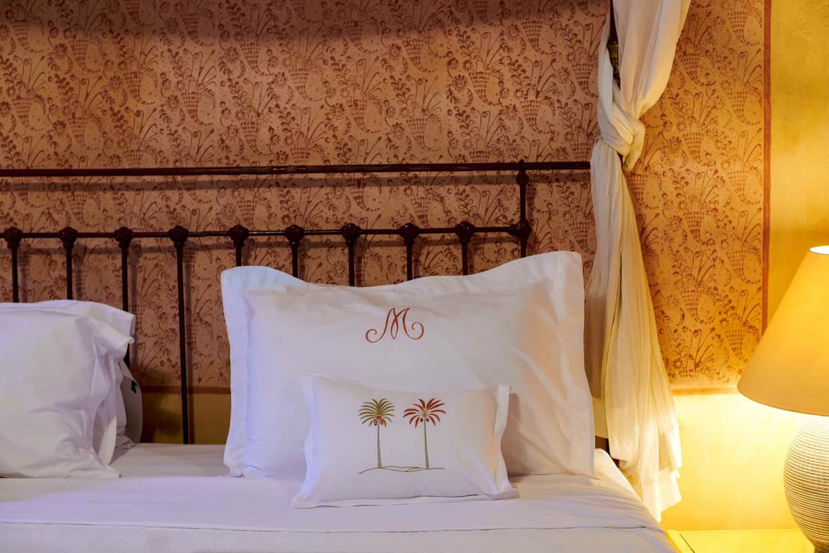 A bed with white linens, two decorative pillows with palm tree designs, and a canopy.
