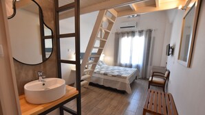 Un dormitorio con cama de madera, lavamanos blanco, banco de madera, escalera y un espejo grande.