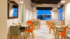 Un comedor con varias mesas y sillas, ventanas amplias y un equipo de aire acondicionado.
