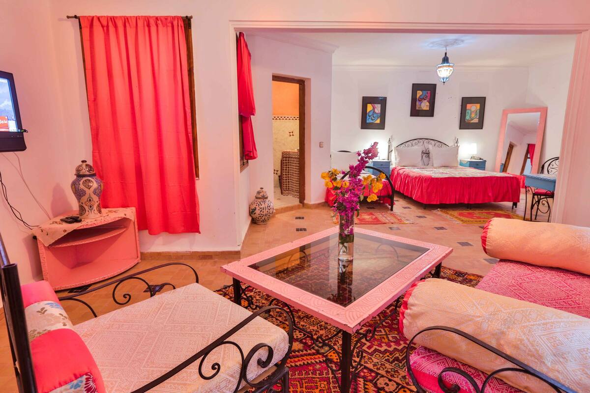 A room with a bed, a table with a vase, a chair, and a sofa.