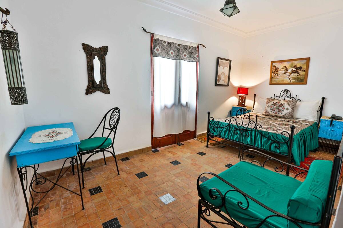 A bedroom with a bed, a chair, a table, and a window with curtains.