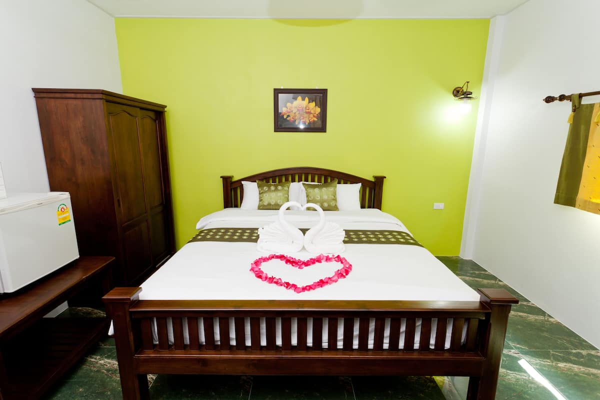 A neatly made bed with a heart-shaped decoration, a wooden wardrobe, and a small refrigerator.