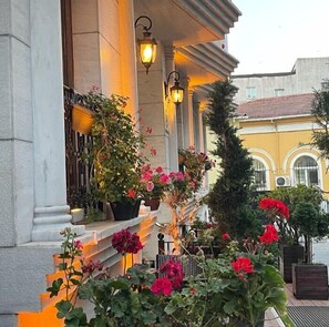 Stunning classical building with columns and a charming balcony featuring lush greenery and potted plants.