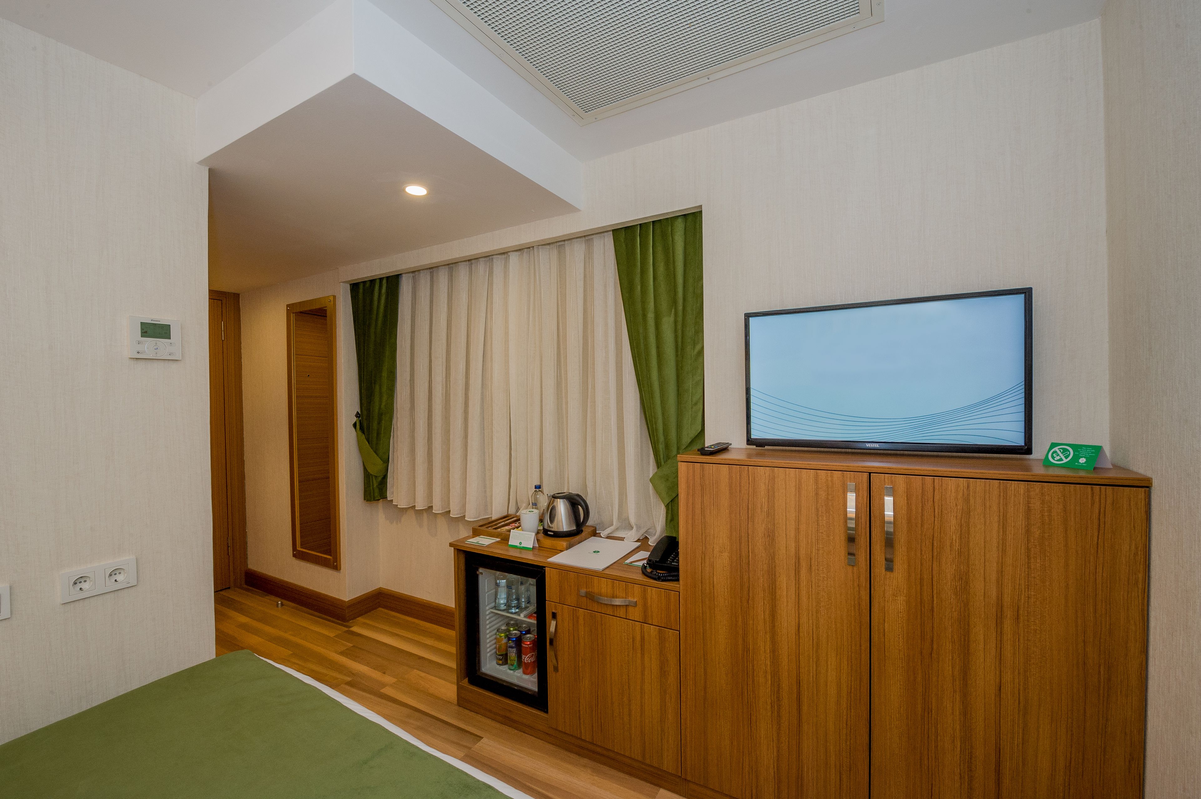 Une chambre d’hôtel avec un meuble en bois, une télévision, un minibar et une moquette verte.
